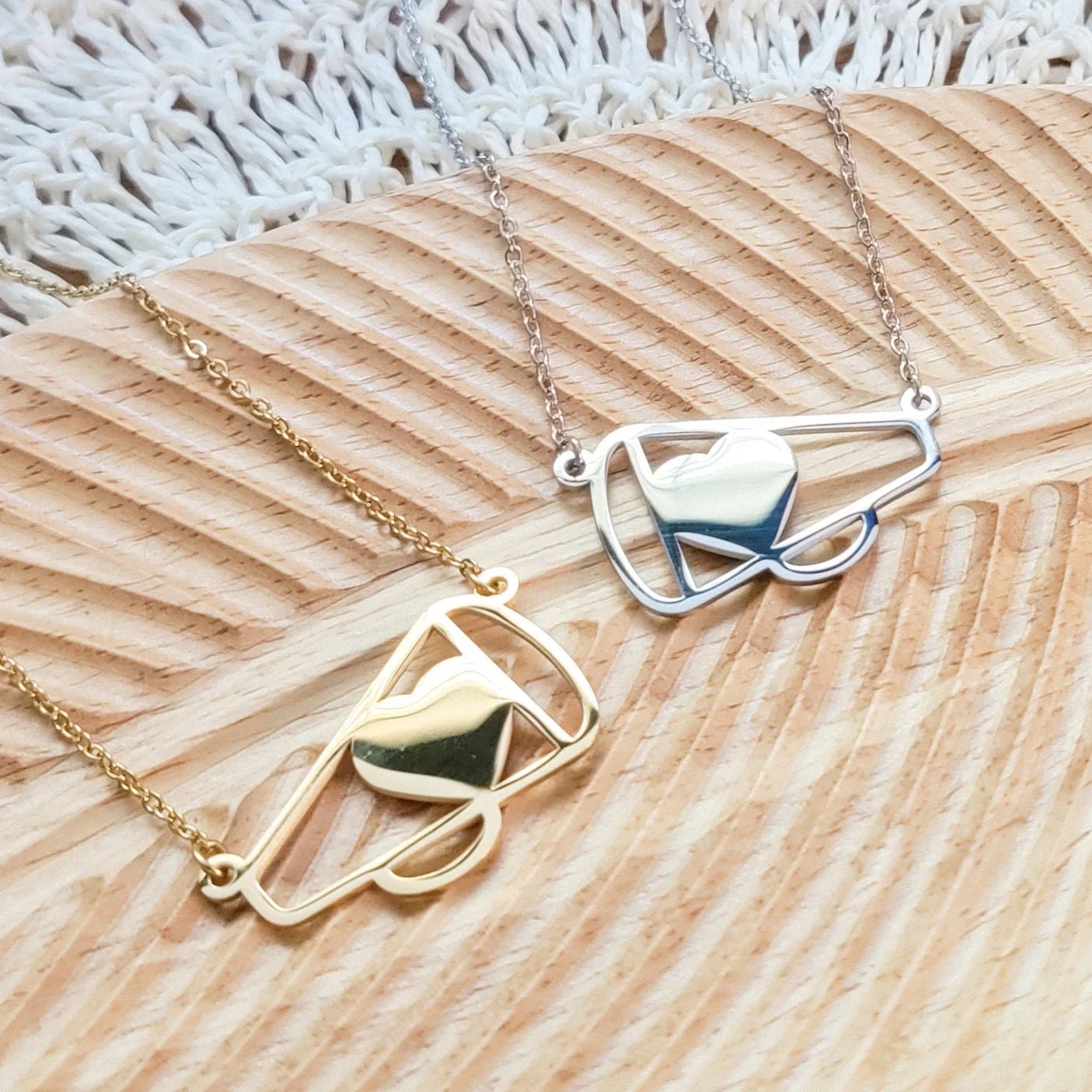 Two necklaces, one gold and one silver, on a textured wooden surface.