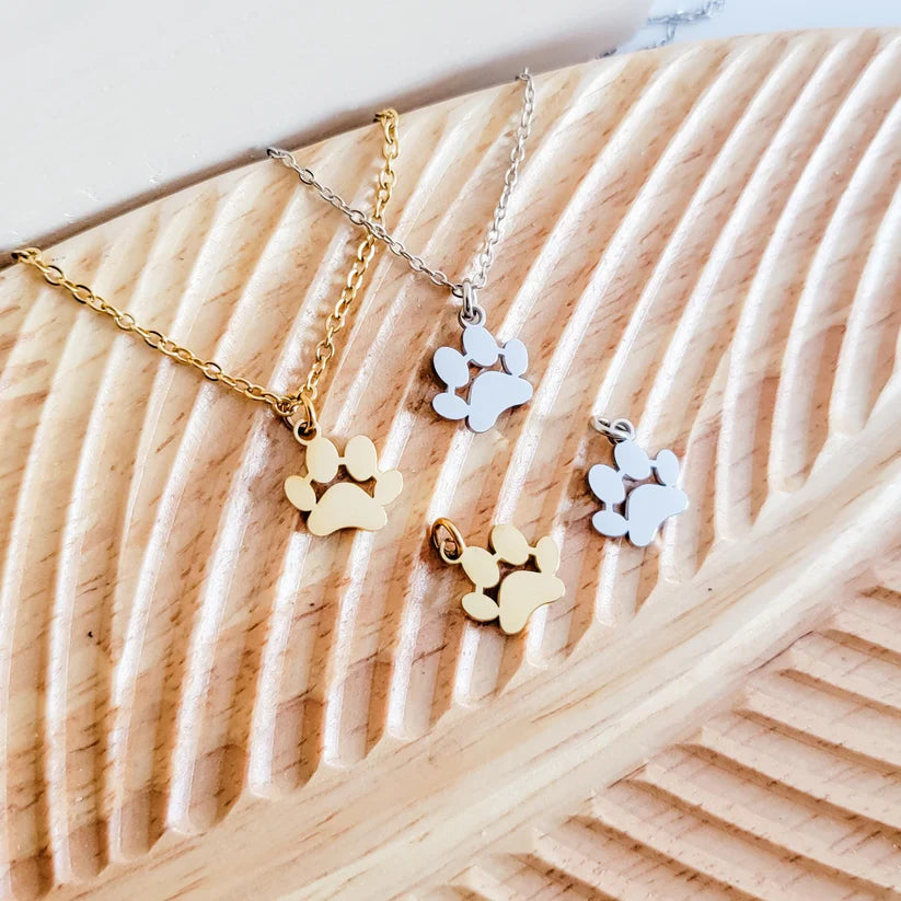 Three paw-shaped pendants on gold and silver chains on a wooden surface.